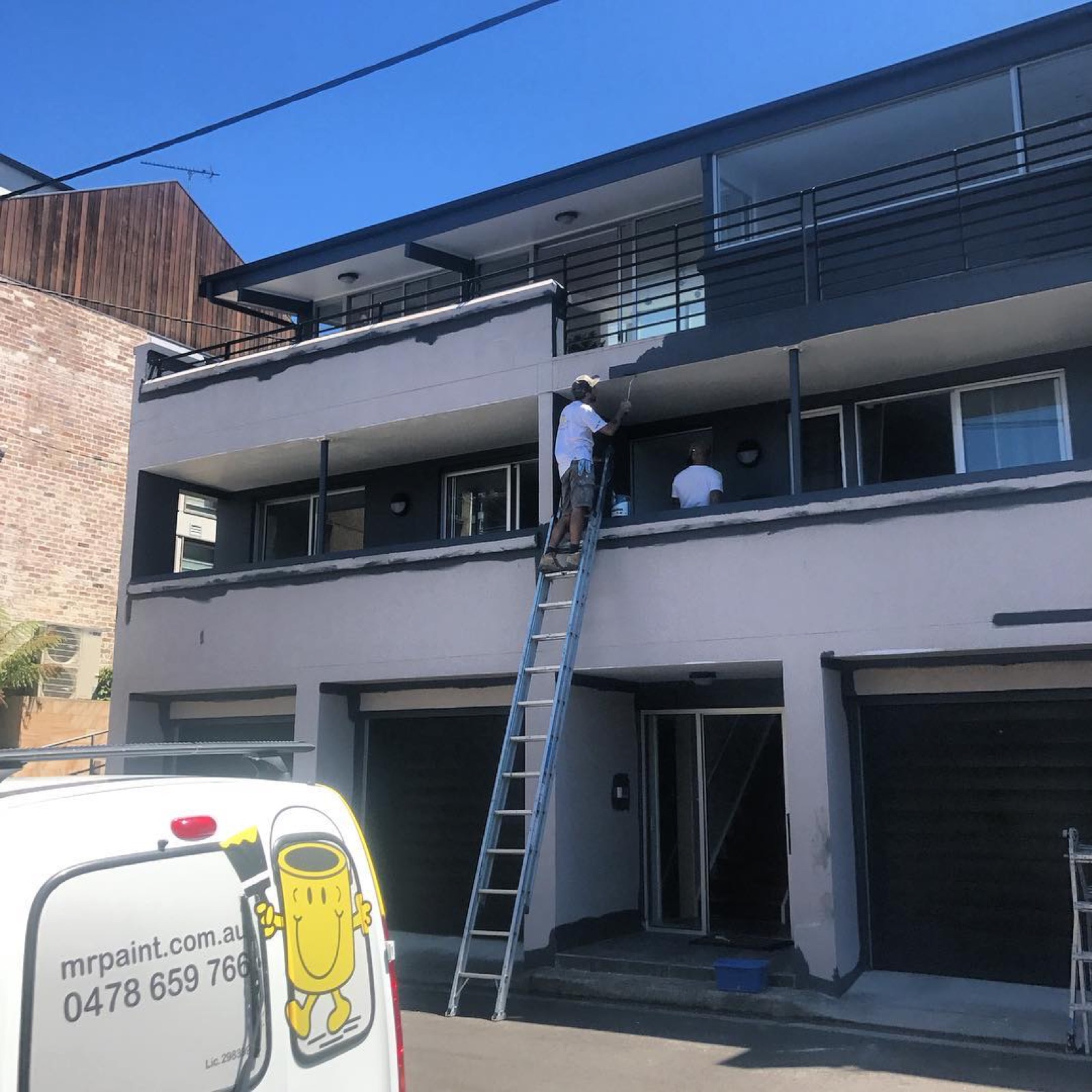 Painter on a tall ladder on a modern townhouse facade